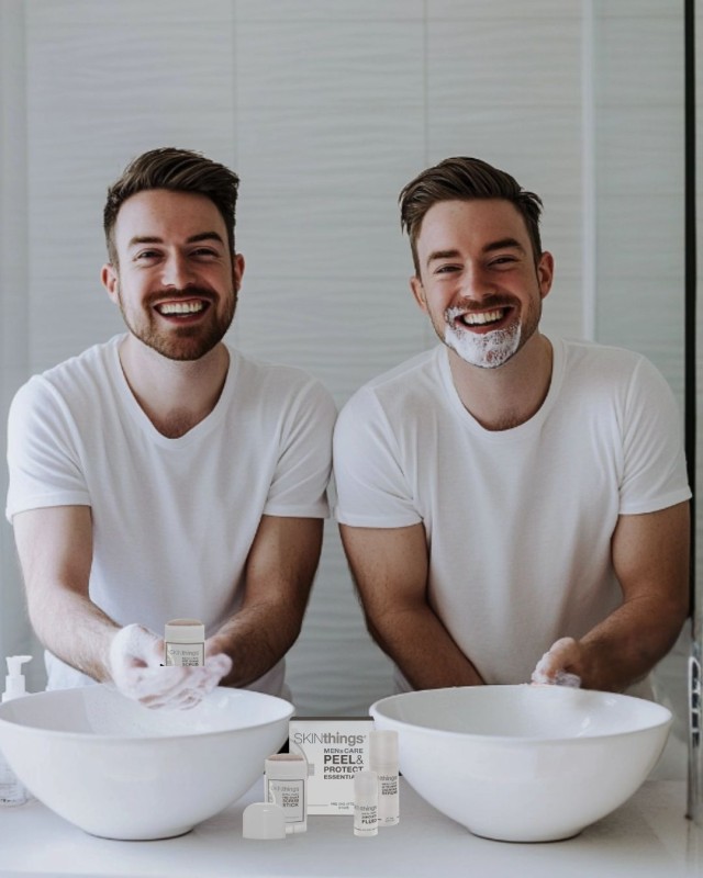 Peel-Protect-Set-maennliche-Zwillinge-Bart-dunkle-kurze-Haare-stehen-im-Badezimmer-vor-zwei-runden-Waschbecken-auf-dem-Waschtisch-das-Peel-Protect-Set-der-Linke-Zwilling-haelt-Pre