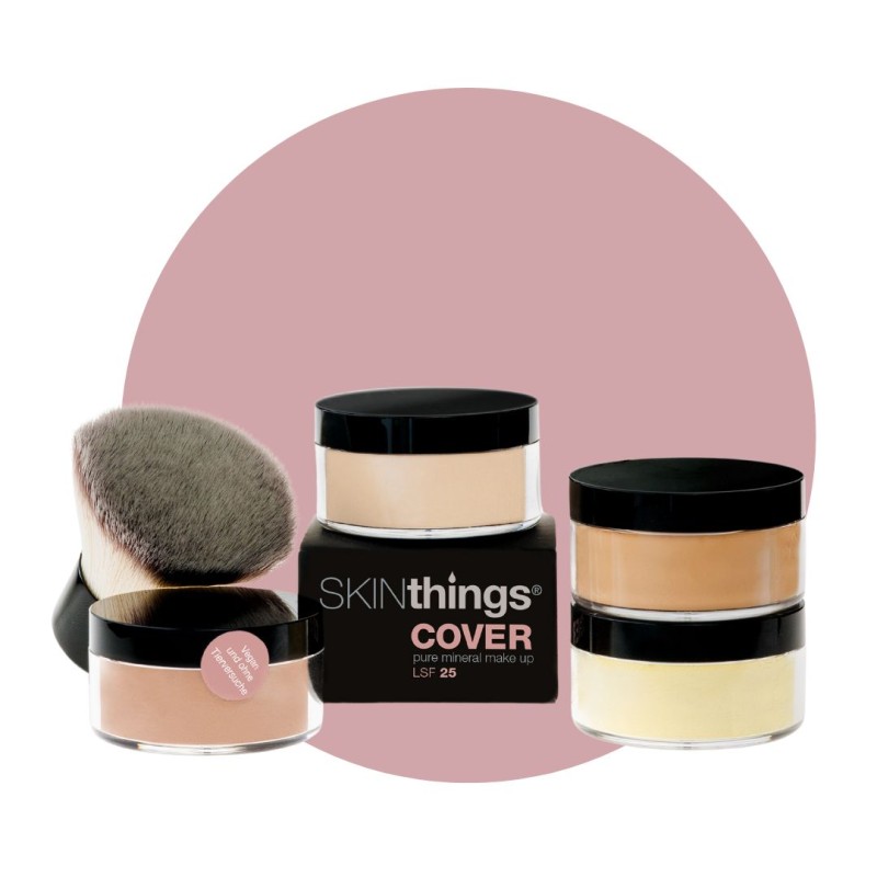 Foto mit vier mit Cover Mineral Make-Up gefüllten Dosen in unterschiedlichen Farbtönen, daneben liegt ein Pinsel, im Hintergrund ist ein rosa Kreis