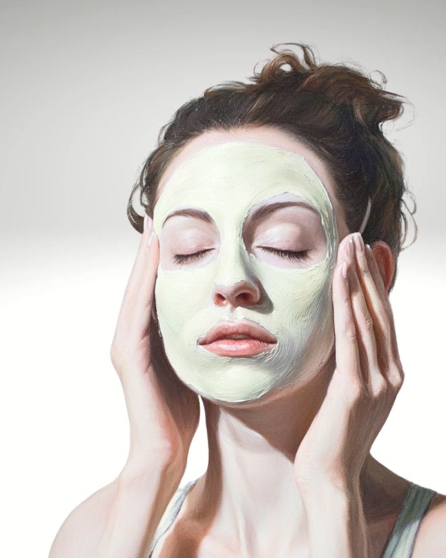 Frau-braune-Haare-zum-Dutt-hocgesteckt-Augen-geschlossen-weisse-Crememaske-auf-Geicht-aufgetragen-beide-Haende-an-der-Schlaefe